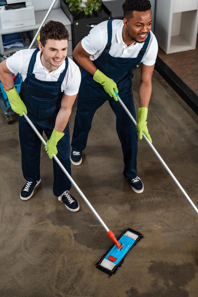 two smiling multicultural cleaners washing floor with mops - Photo, Image