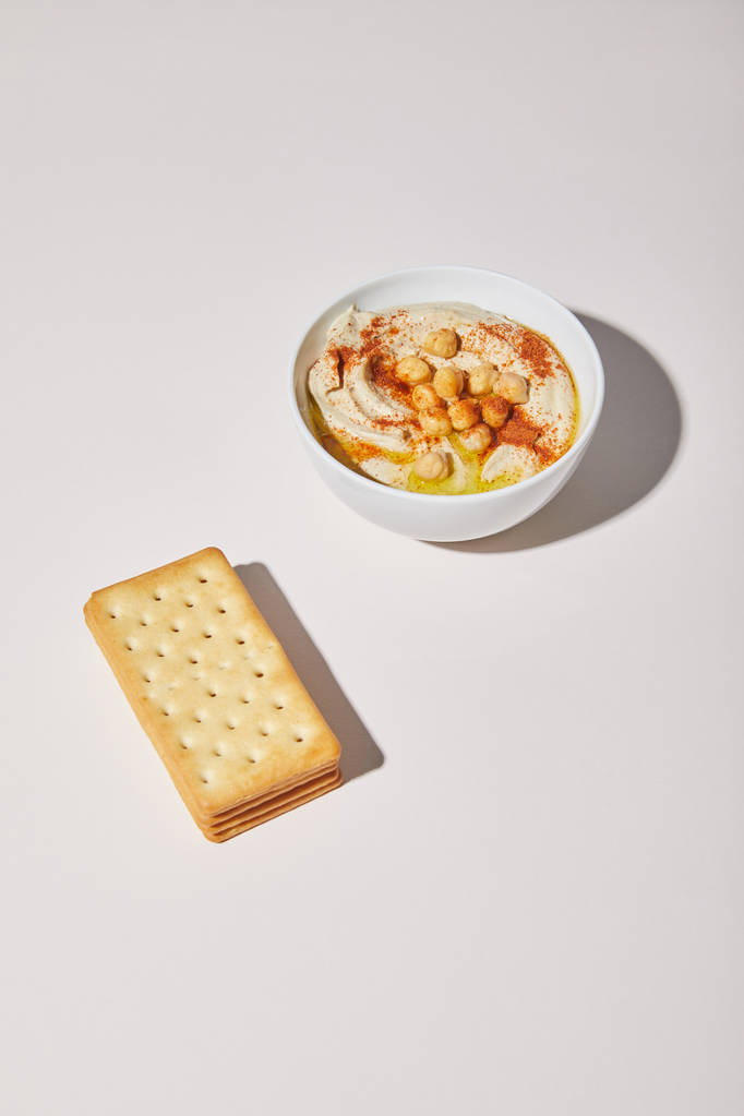 Bowl with tasty hummus and crackers on grey background - Photo, Image