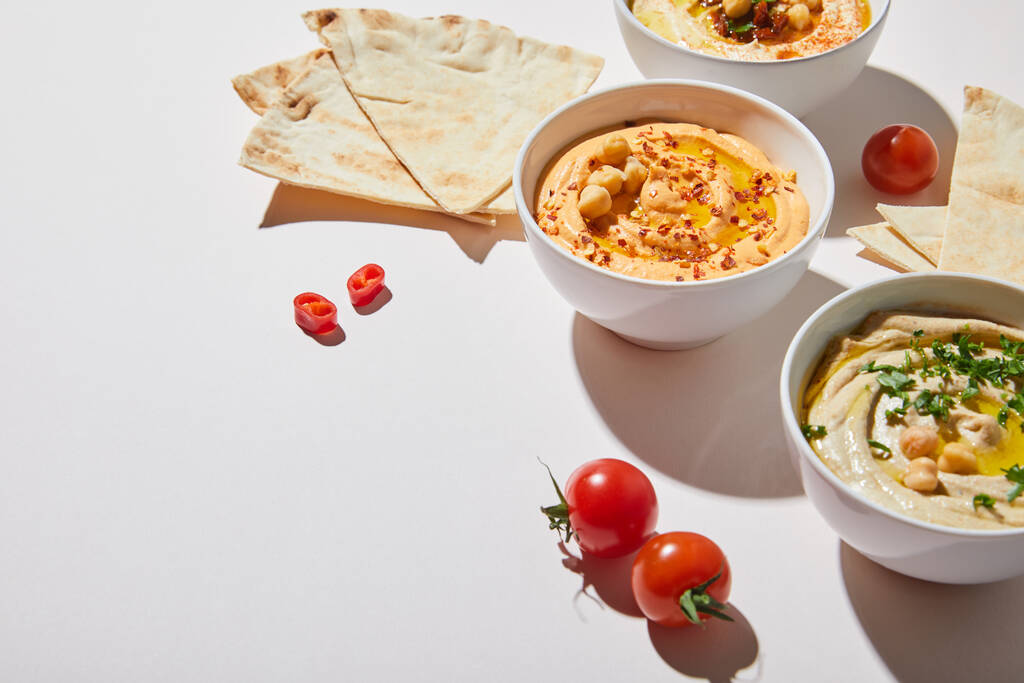 Bowls with delicious hummus, ripe vegetables and pita bread on grey background - Photo, Image