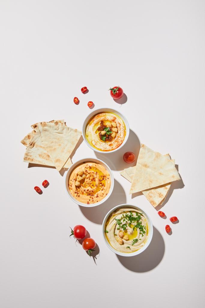 Top view of bowls with delicious hummus, ripe vegetables and pita bread on grey background - Photo, Image