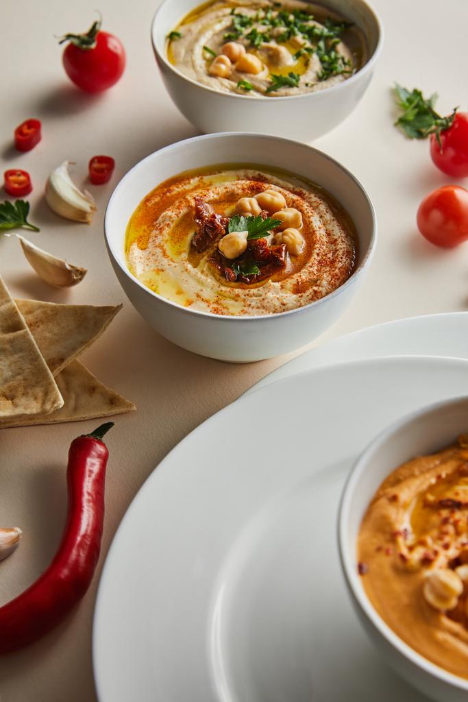 Селективный фокус тарелок, миски с вкусным хумусом, спелые овощи и пита хлеб на сером фоне
 - Фото, изображение
