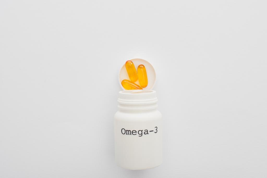 Bovenaanzicht van geopende container met omega-3 capsules op witte achtergrond - Foto, afbeelding