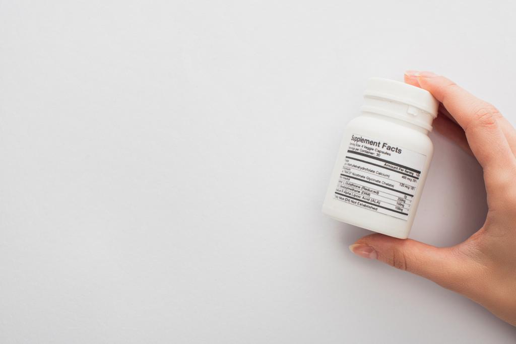 Cropped view of woman holding container with dietary supplements on white  - Photo, Image