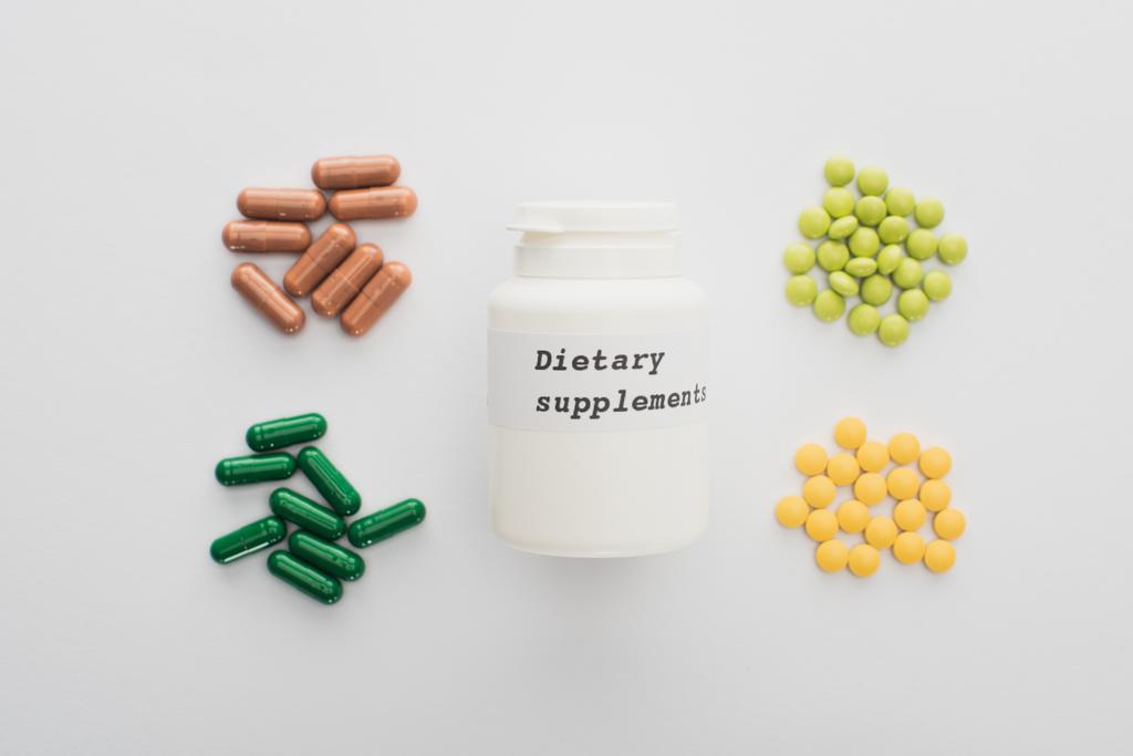 Вид зверху контейнера з дієтичними добавками з таблетками та капсулами на білому тлі
 - Фото, зображення