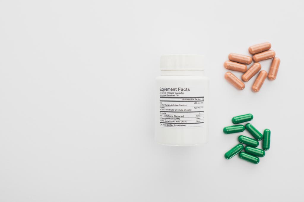 Top view of container with brown and green capsules on white background  - Photo, Image