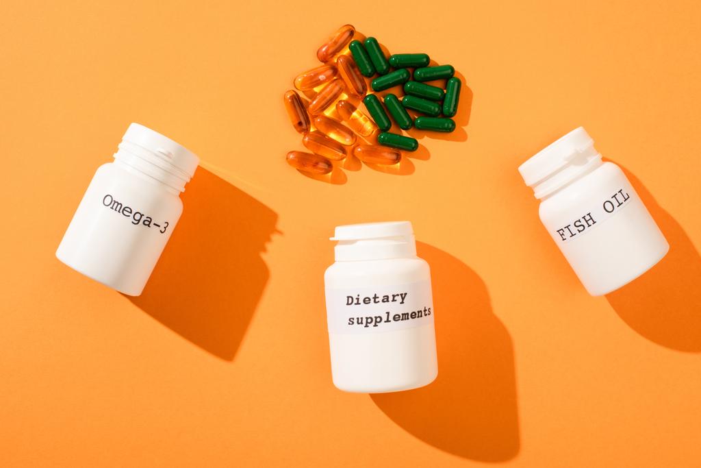 Bovenaanzicht van containers met omega-3, visolie en voedingssupplementen belettering met capsules op oranje - Foto, afbeelding