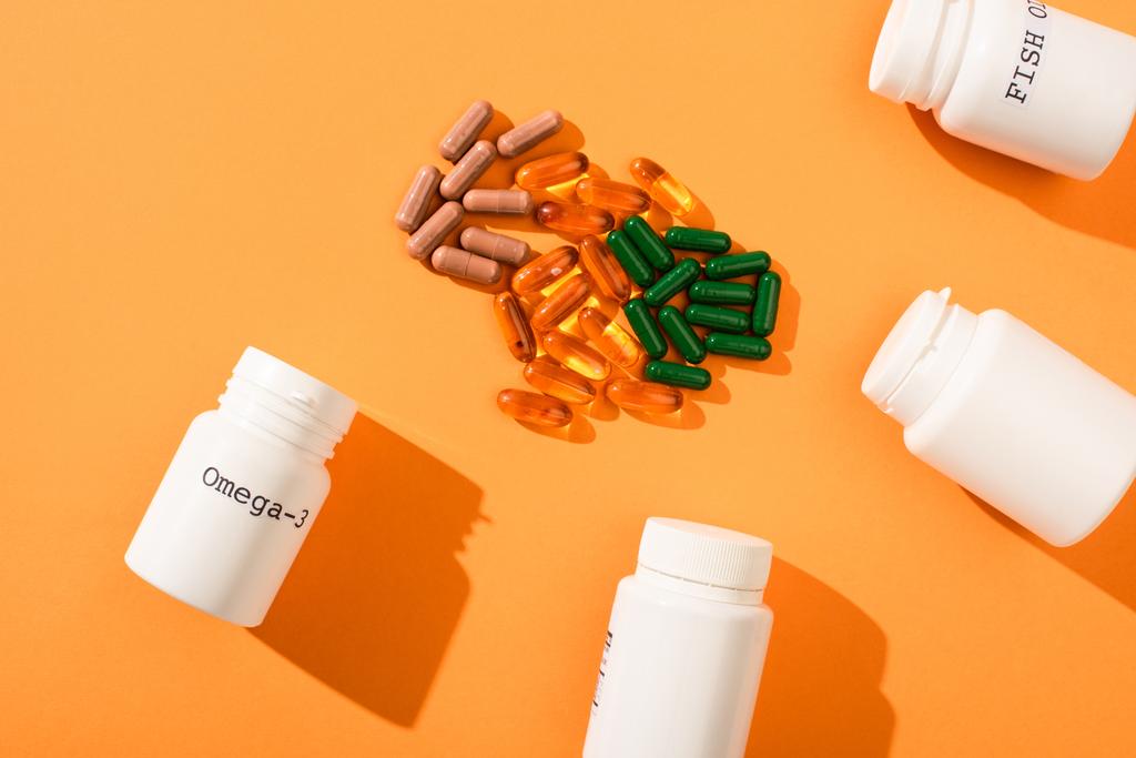 Top view of containers with omega-3 and fish oil lettering near capsules on orange background - Photo, Image