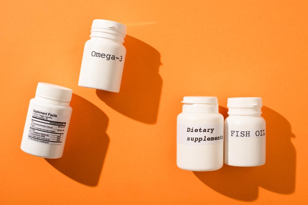 Draufsicht auf Behälter mit Omega-3, Fischöl und Nahrungsergänzungsmitteln Schriftzug auf orangefarbenem Hintergrund - Foto, Bild