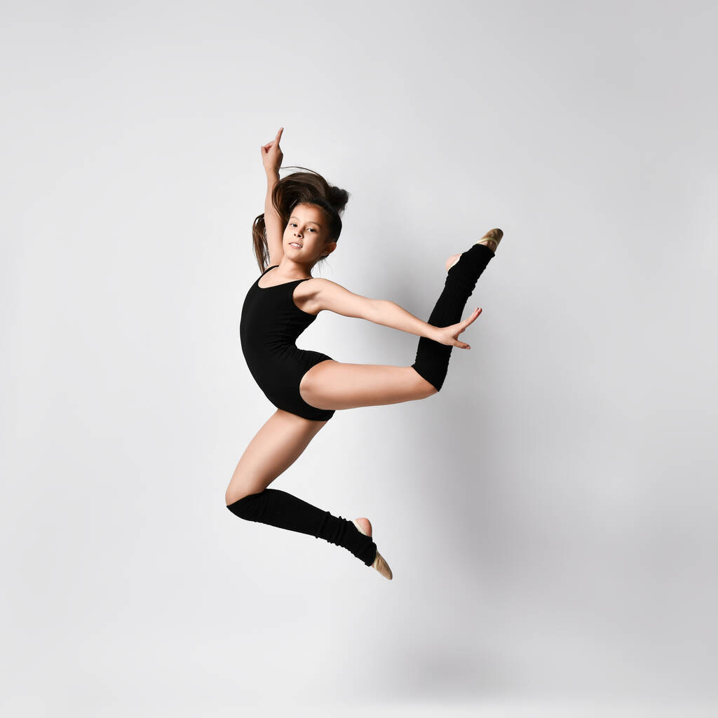 Teenage brunetka dívka gymnastka s culíkem, v černém trikotu, kolena ponožky a baletní boty, provádění cvičení, pózování izolované na bílém. Detailní záběr. - Fotografie, Obrázek