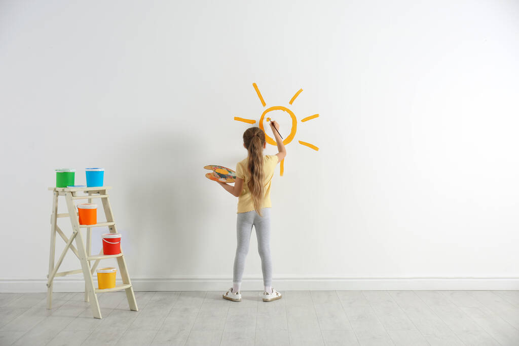 Little child painting sun on white wall indoors - Photo, Image