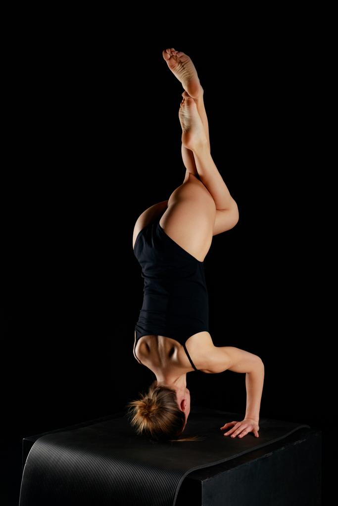 κορίτσι σε bodysuit κάνει αετός πόδια handstand άσκηση απομονώνονται σε μαύρο  - Φωτογραφία, εικόνα
