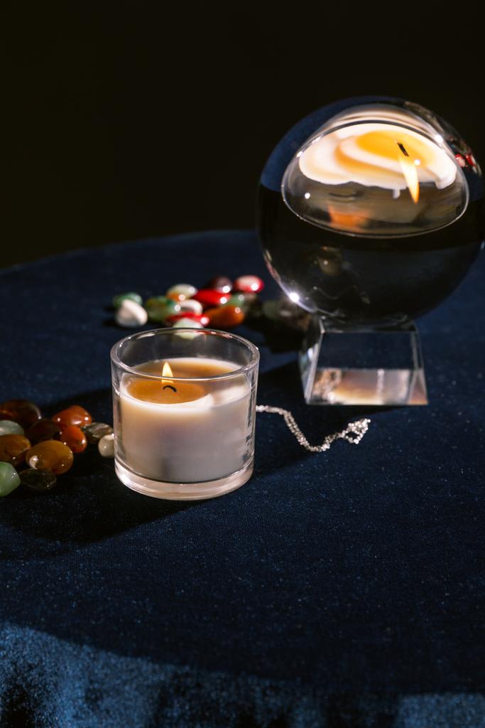 Selektivní zaměření křišťálové koule, svíčky, věštecké kameny na tmavě modré sametové tkanině izolované na černé - Fotografie, Obrázek
