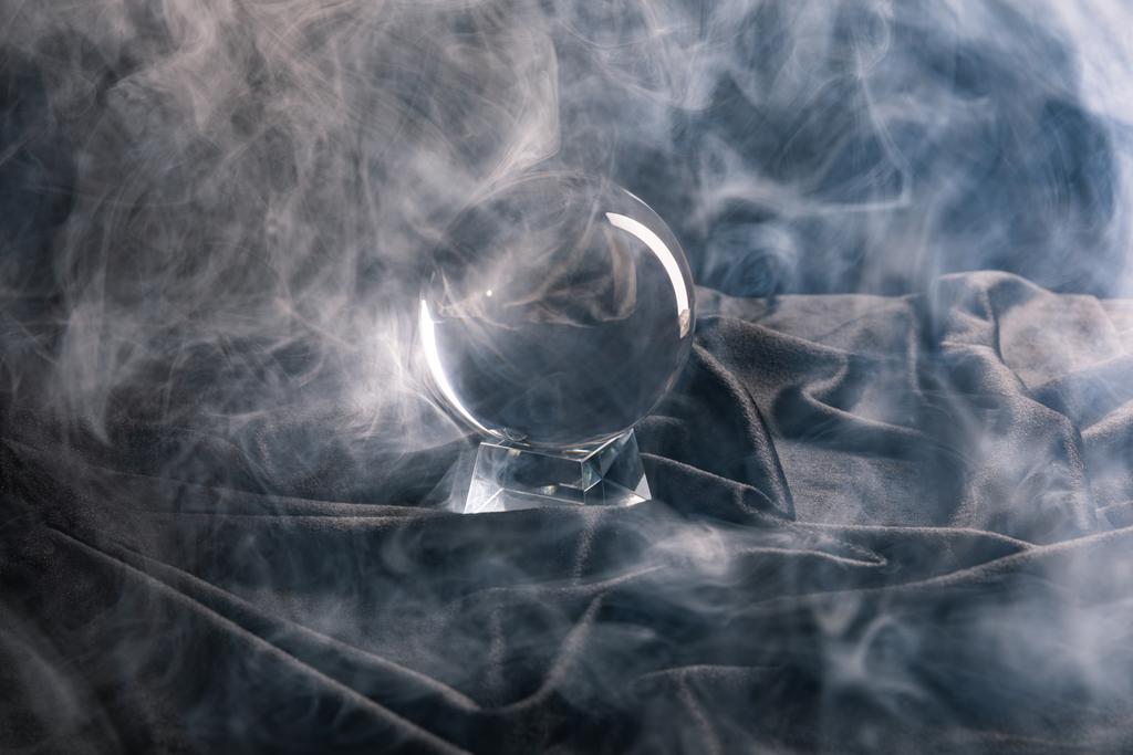 Bola de cristal sobre têxteis com fumaça em torno de fundo escuro
 - Foto, Imagem