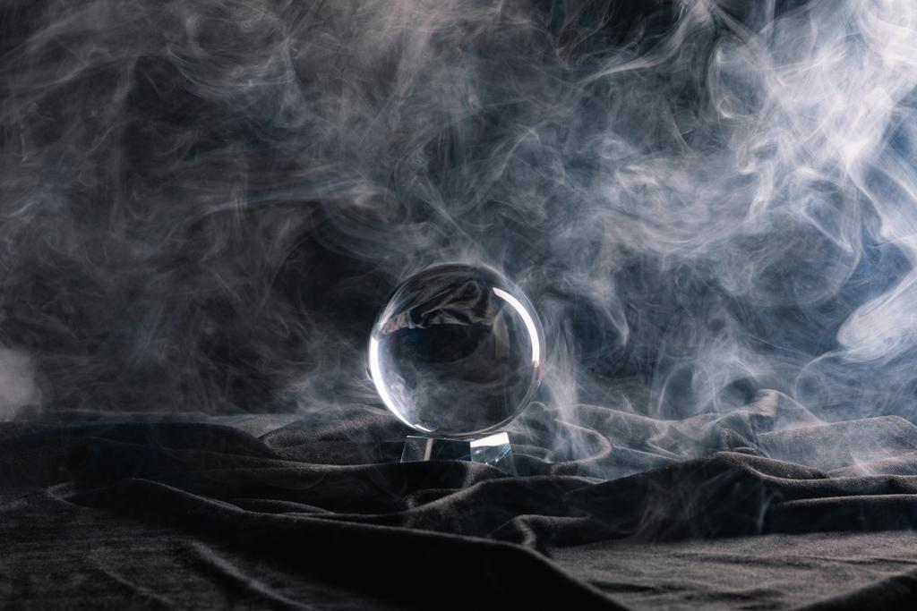 Crystal ball on black textile with smoke on dark background - Photo, Image