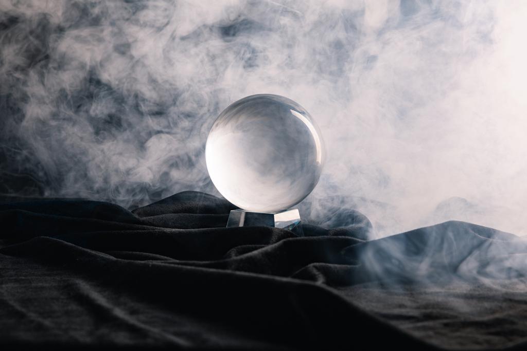 Kristallkugel auf Textil mit Rauch auf dunklem Hintergrund - Foto, Bild