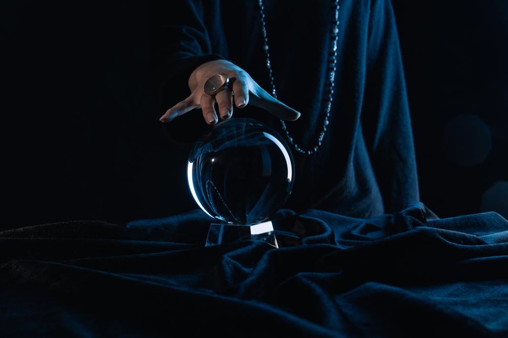 Обрезанный вид женской руки, касающейся хрустального шара на черном фоне
 - Фото, изображение
