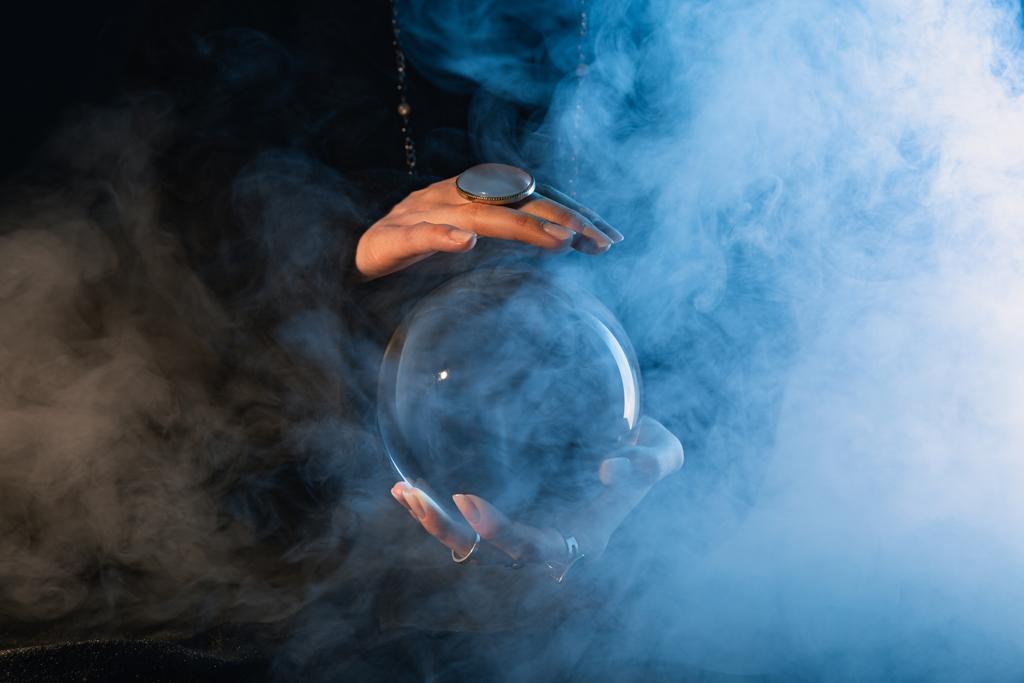 Kristal küreli kadın ellerinin kısmi görüntüsü ve koyu mavi etrafında duman.  - Fotoğraf, Görsel
