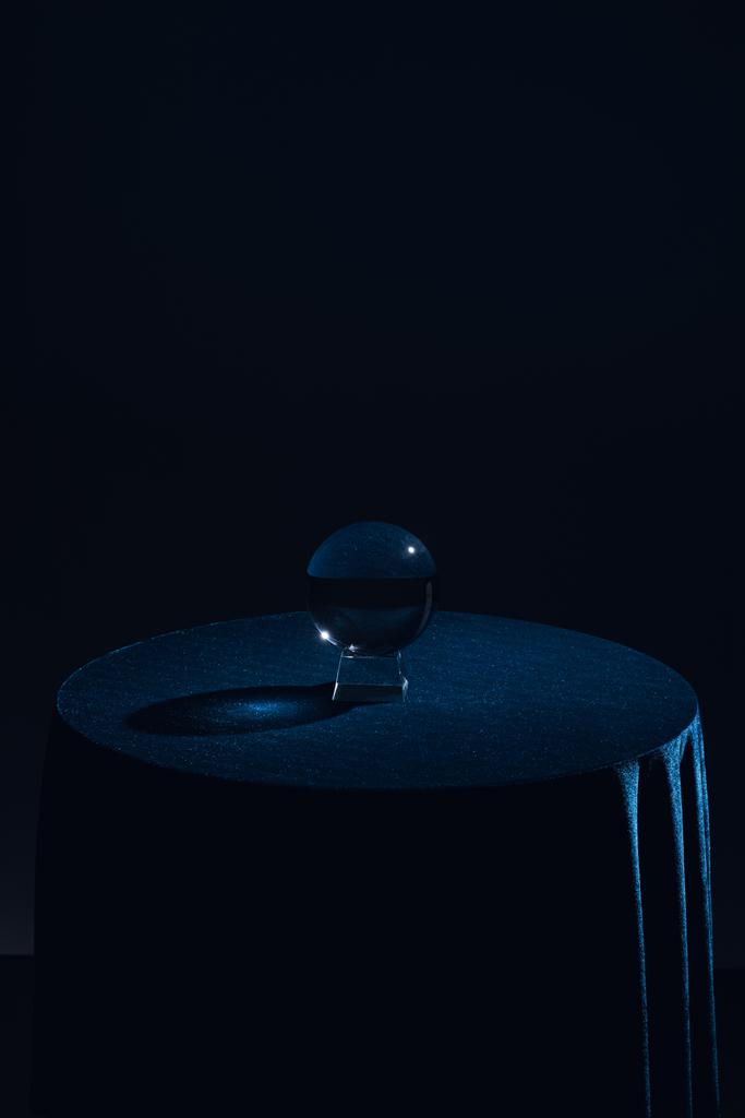 Kristallkugel auf rundem Tisch mit dunkelblauer Tischdecke auf schwarzem Hintergrund - Foto, Bild