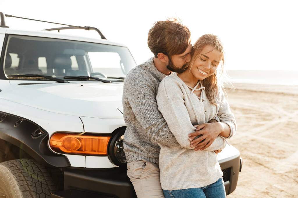 Foto de jovem alegre casal amoroso ao ar livre na praia perto de abraços de carro
. - Foto, Imagem