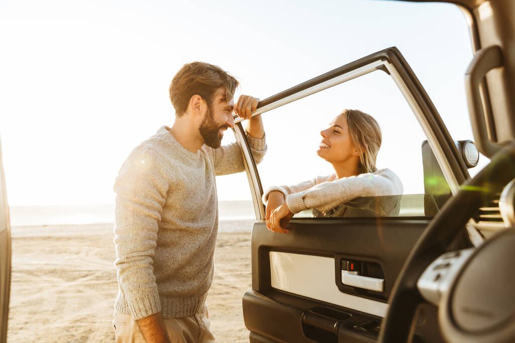 Kuva hymyilevä tyytyväinen rakastava pari ulkona rannalla lähellä autoa
. - Valokuva, kuva