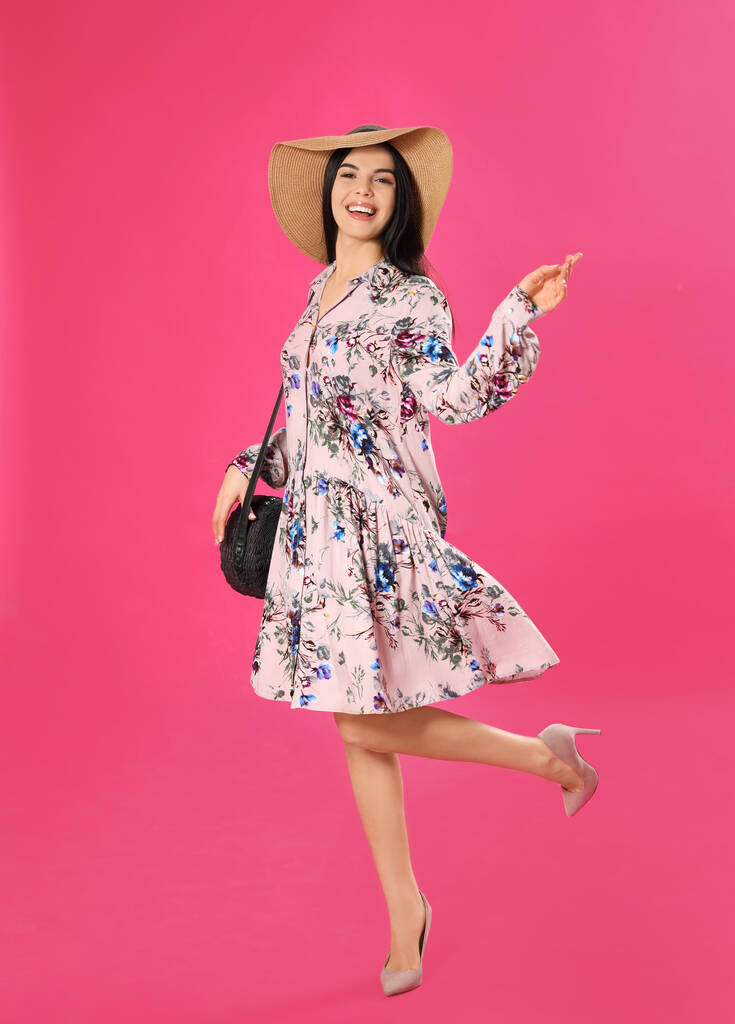 Nuori nainen yllään kukka tulostaa mekko ja olki hattu vaaleanpunainen tausta
 - Valokuva, kuva