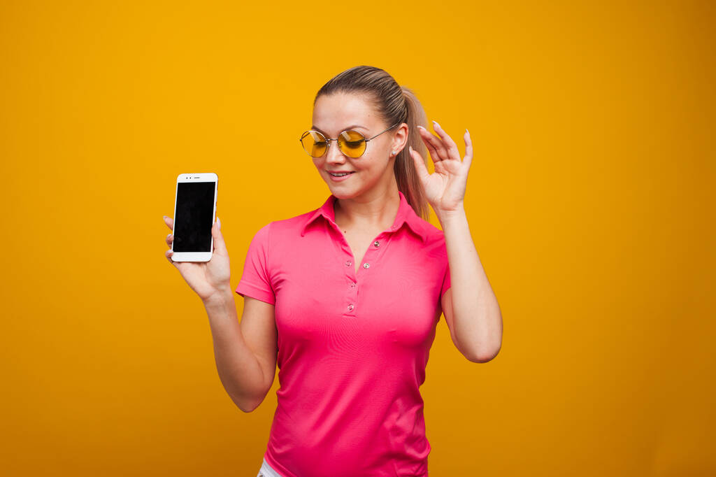 Jasna i pozytywna młoda kobieta ze smartfonem na żółtym tle. Dziewczyna używa smartfona. - Zdjęcie, obraz