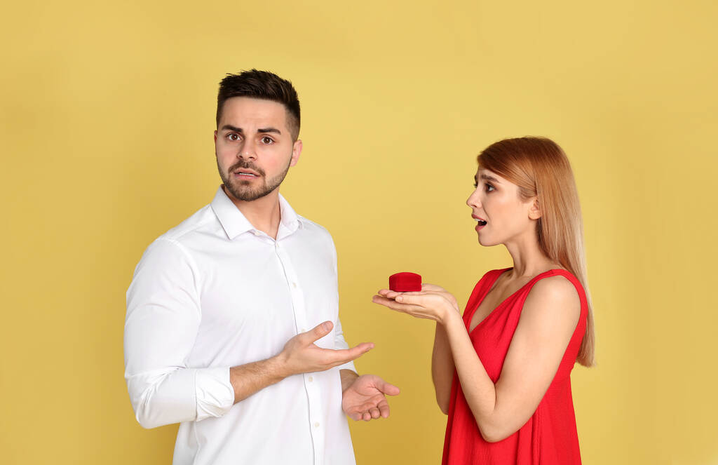 Молодая женщина с обручальным кольцом делает предложение о браке со своим парнем на жёлтом фоне
 - Фото, изображение