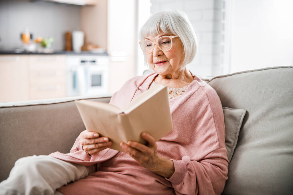 Senior woman in glasses reading book at home - Photo, Image
