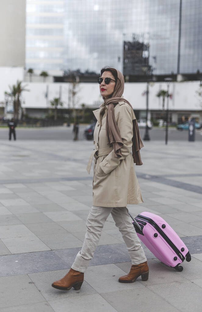 Başörtüsü ve bavulu olan çekici bir Arap kadın istasyona doğru yürüyor. - Fotoğraf, Görsel