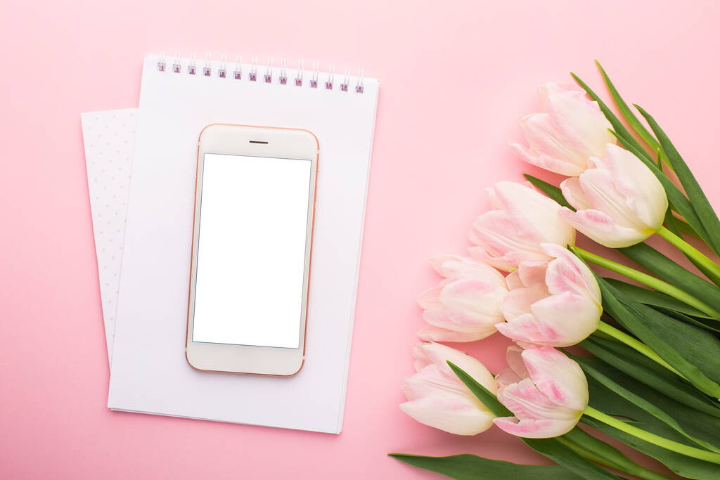 Mobiele telefoon, notebook en lentebloem roze tulpen op de roze achtergrond. Thema van de liefde, Moederdag, vrouwen dag plat lag bovenaanzicht - Foto, afbeelding