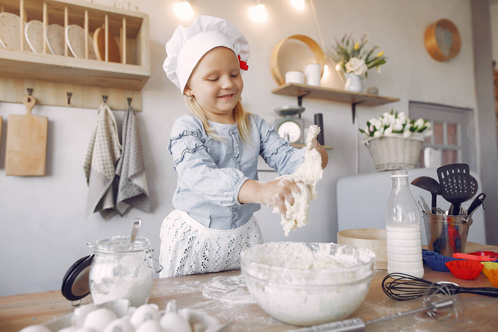 Маленькая девочка в белой шляпе шеф-повара готовит тесто для печенья
 - Фото, изображение