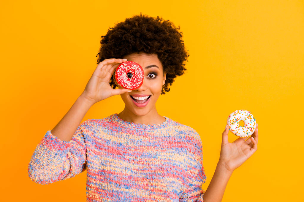 Portrait amazed excited afro american girl hold two tasty delicious donuts close cover eyes make imagine humor joke binoculars wear colorful jumper isolated yellow bright color background - Photo, Image