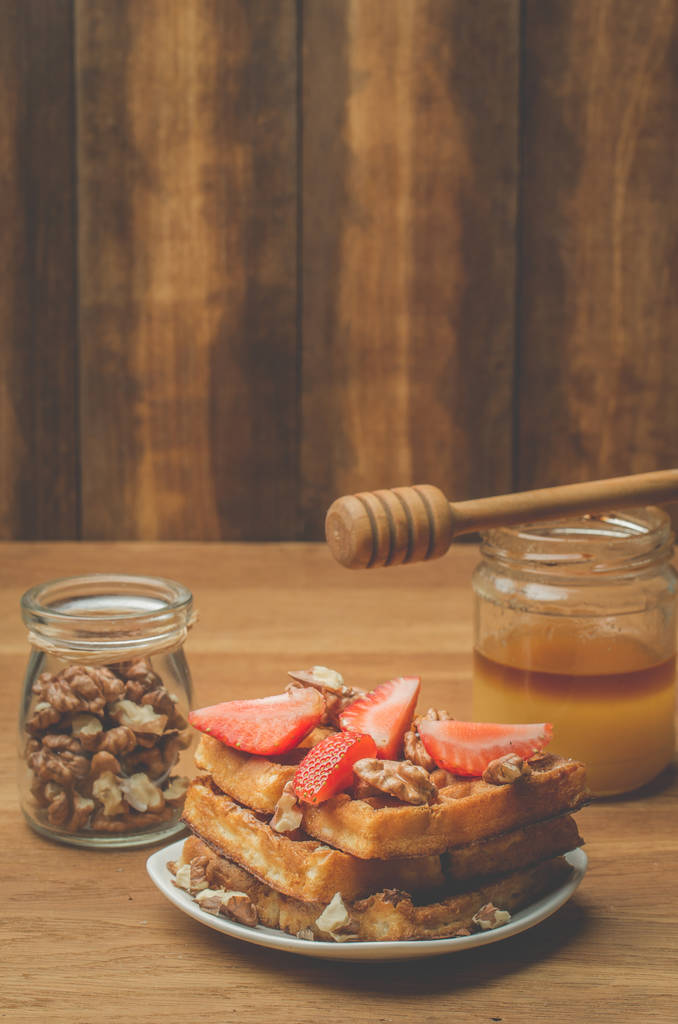 Кувшин меда с медовой ковшой и домашние вафли украшены клубникой и грецким орехом на деревянном фоне. Селективный фокус
 - Фото, изображение