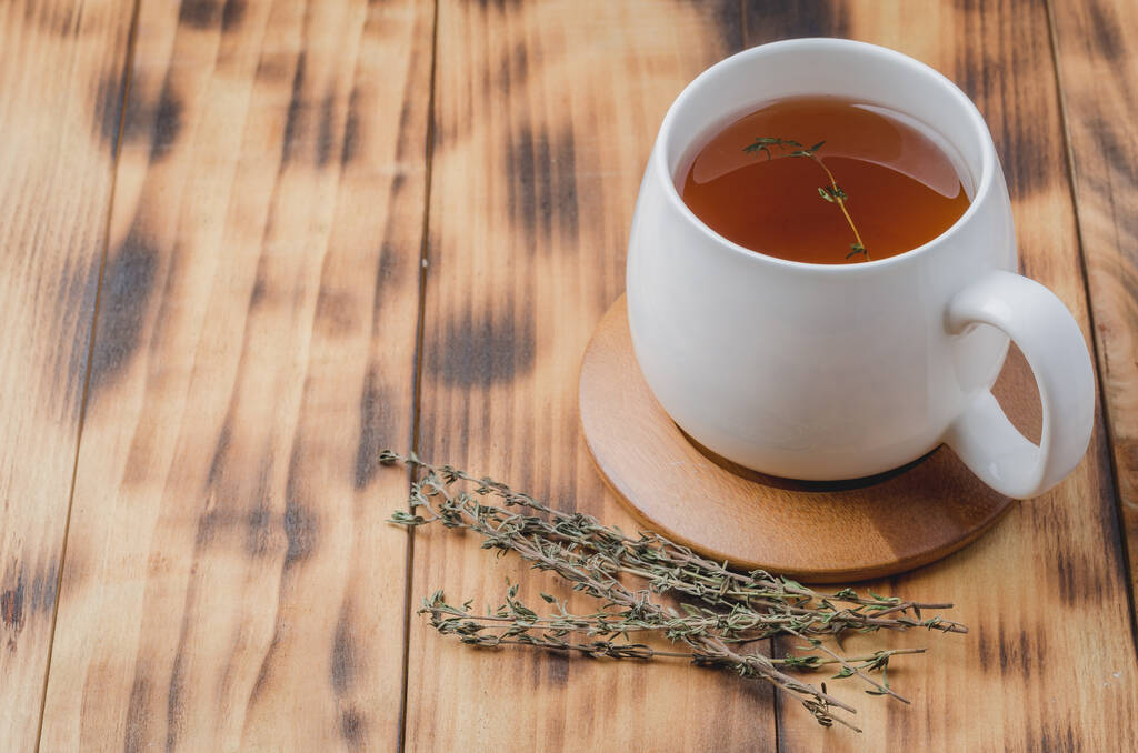 Тимьяновый травяной чай в белой чашке на бамбуковой опоре на деревянном столе. Copyspace
 - Фото, изображение