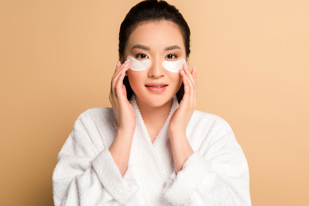 belle femme asiatique en peignoir avec des patchs sur le visage sur fond beige
 - Photo, image