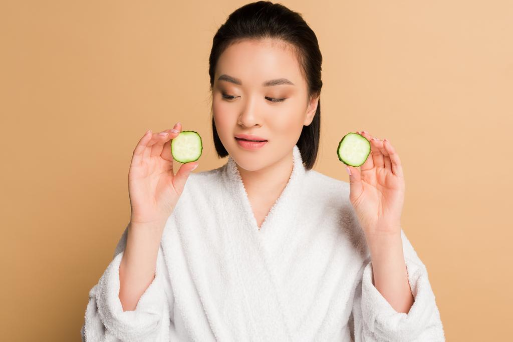 beautiful asian woman in bathrobe with cucumber slices on beige background - Photo, Image
