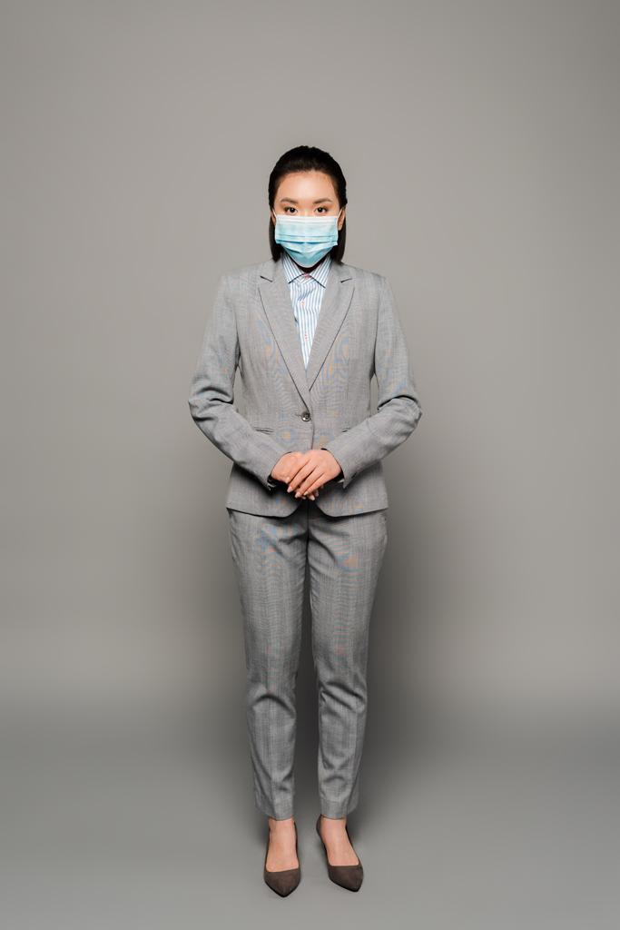 νεαρή επιχειρηματίας με ιατρική μάσκα σε γκρι φόντο - Φωτογραφία, εικόνα