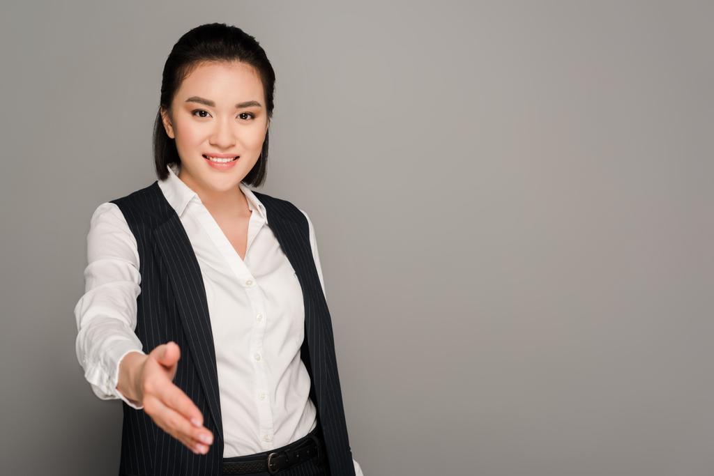 usmívající se mladá podnikatelka dává ruku na šedém pozadí - Fotografie, Obrázek