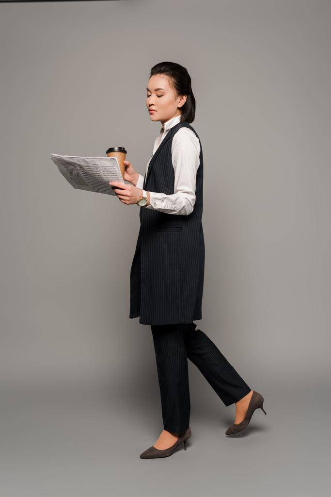 giovane donna d'affari che legge giornale e beve caffè su sfondo grigio
 - Foto, immagini