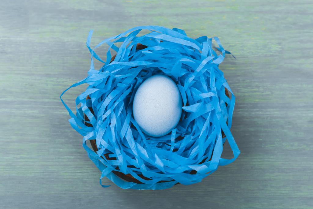 Horní pohled na hnízdo s malovaným kuřecím vejcem na dřevěném pozadí, velikonoční koncept - Fotografie, Obrázek