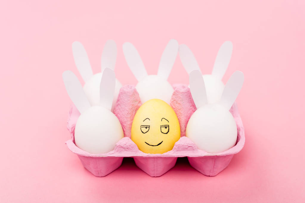 Dekorativní králíci a žluté vejce s usmívajícím se obličejovým výrazem na růžové, velikonoční koncepci - Fotografie, Obrázek