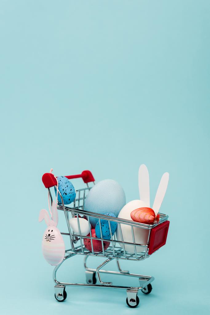 Ovos de páscoa coloridos e coelhos decorativos no carrinho em azul
  - Foto, Imagem