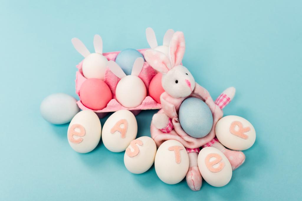 Painted chicken eggs with easter lettering and decorative bunnies on blue background - Photo, Image