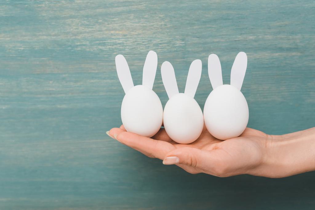 Vista recortada de la mano femenina con conejos decorativos de Pascua sobre fondo de madera
 - Foto, Imagen
