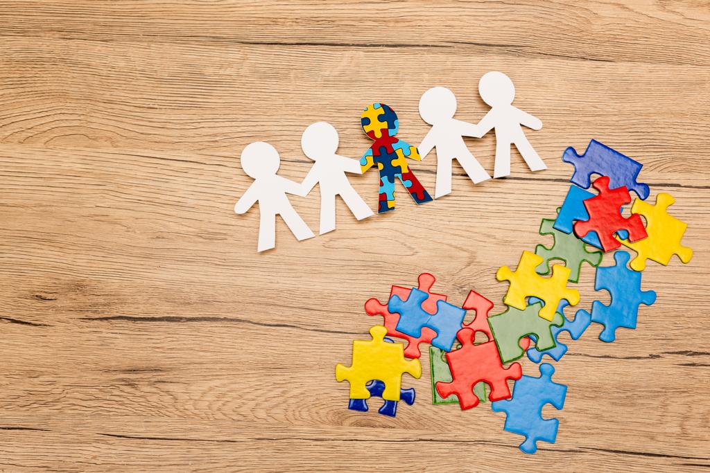 Vista de alto ângulo de criança especial com autismo entre outros e peças de quebra-cabeça em fundo de madeira
 - Foto, Imagem