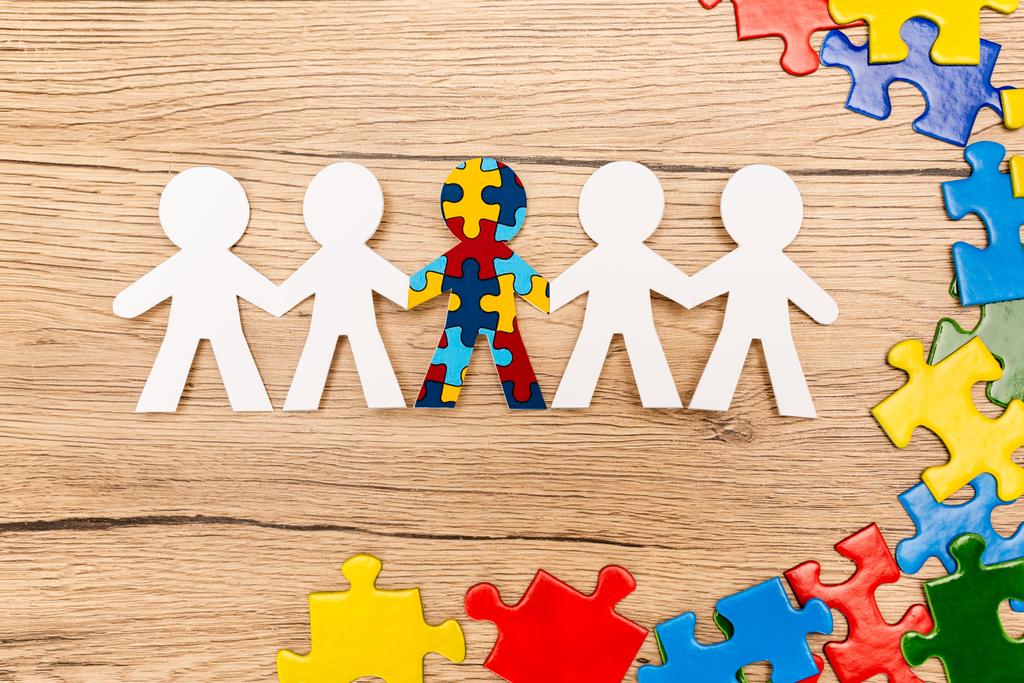 Top view of special kid with autism among another and pieces of multicolored puzzle on wooden background - Photo, Image