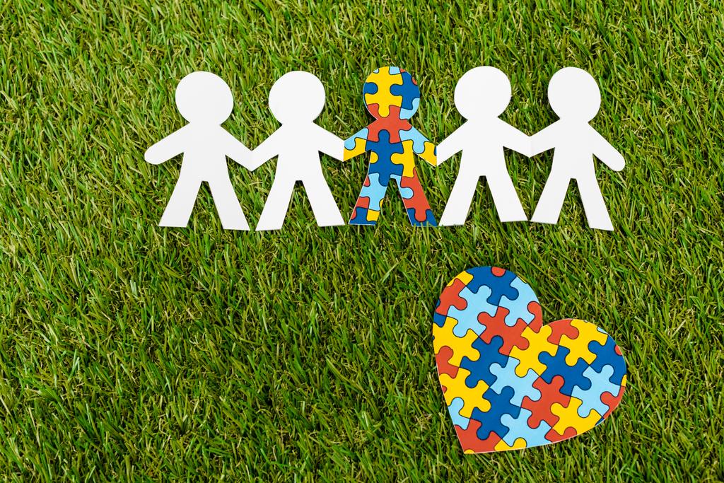 Vista superior de niño especial con autismo entre otro y corazón rompecabezas decorativo sobre fondo verde
 - Foto, imagen