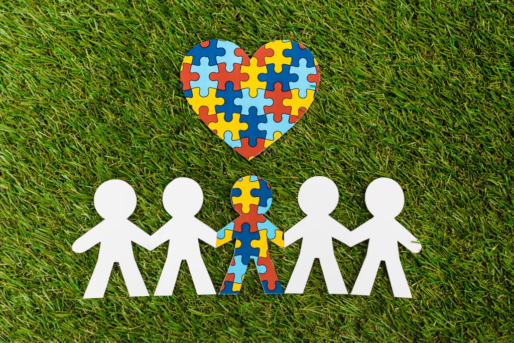 Top pohled na speciální dítě s autismem mezi další a dekorativní puzzle srdce na zelené - Fotografie, Obrázek