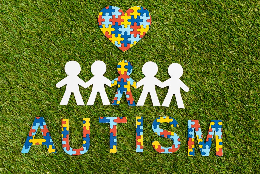 Вид зверху на аутизм написання головоломки, декоративне серце і особлива дитина один з одним на зеленому
 - Фото, зображення