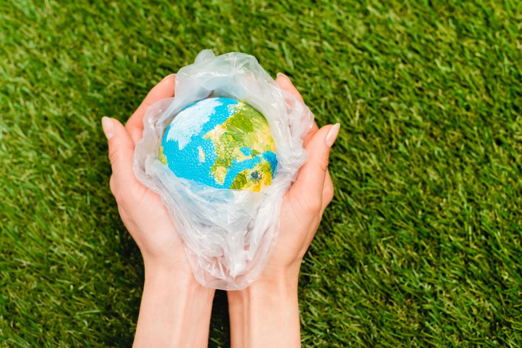 Vue recadrée du sac en plastique avec globe dans les mains des femmes sur vert, concept de réchauffement climatique
 - Photo, image